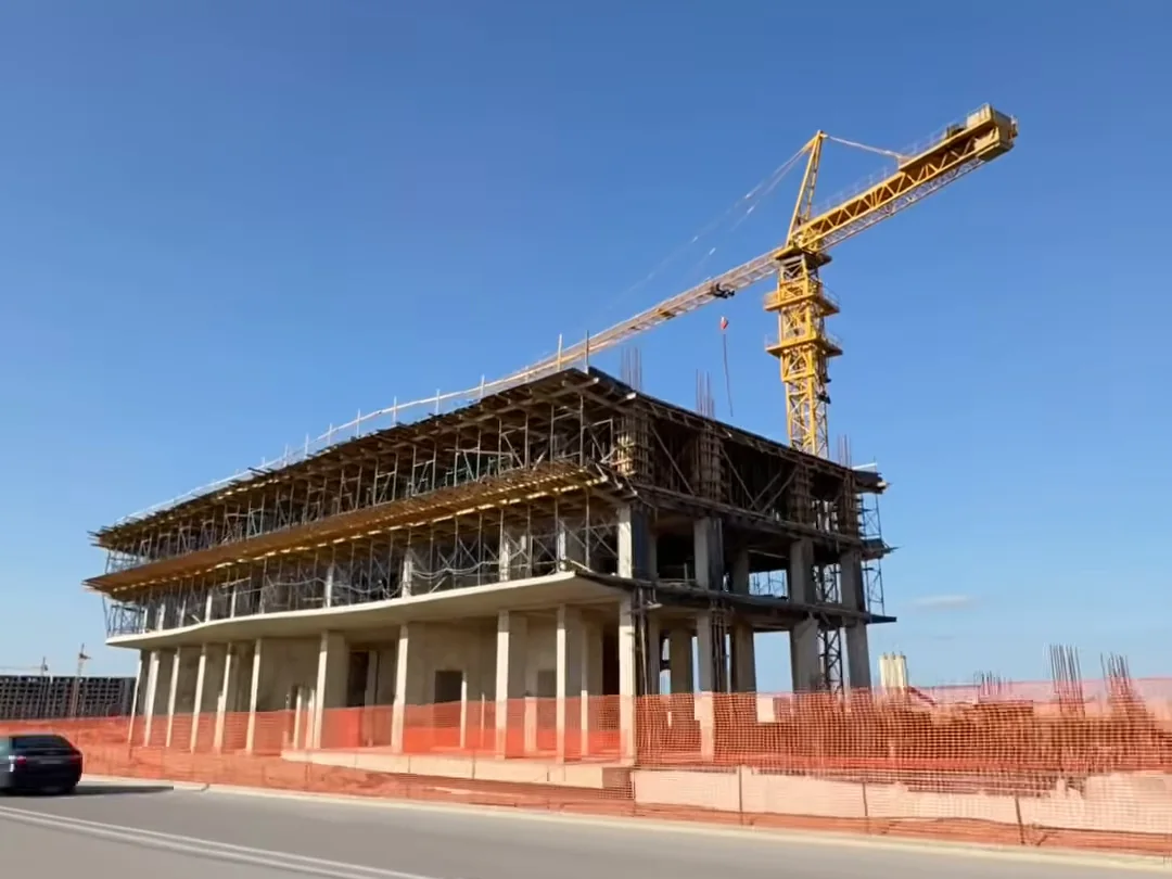 Корпус в лесах и башенный кран, вид с дороги, 21.05.2026